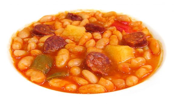 Cuenco de alubias blancas con rodajas de chorizo, patata y pimientos en salsa roja de pimentón