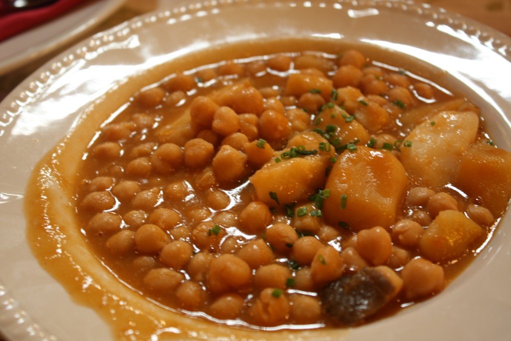 Cuenco de potaje de garbanzos con patata en caldo espeso, espolvoreado con hierbas frescas
