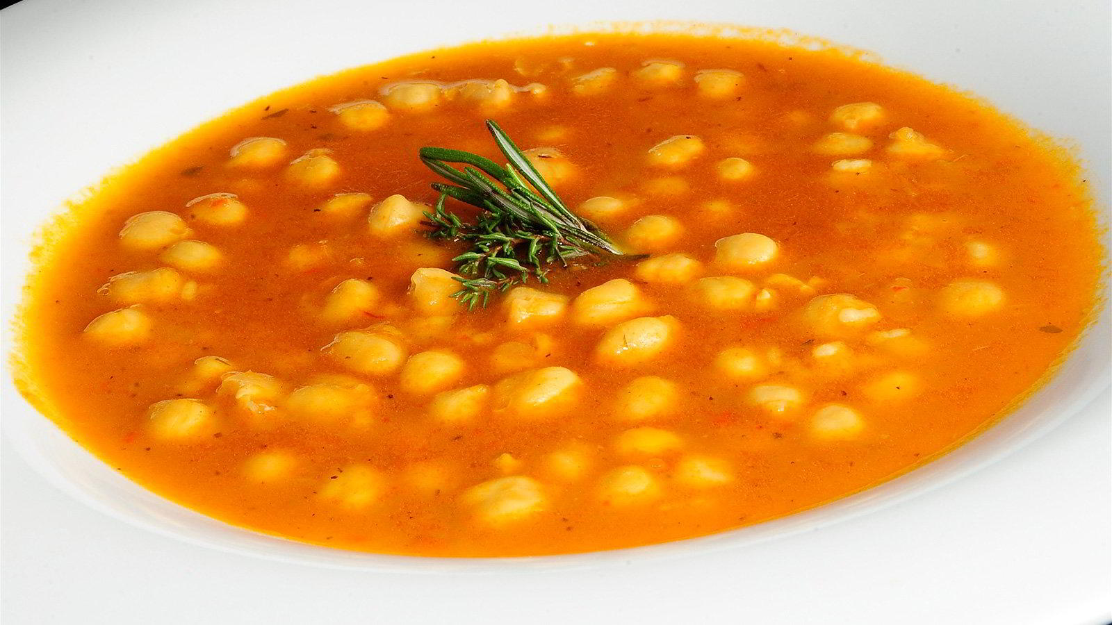 Cuenco de garbanzos en caldo anaranjado de tomate y pimentón, adornado con una ramita de romero y tomillo