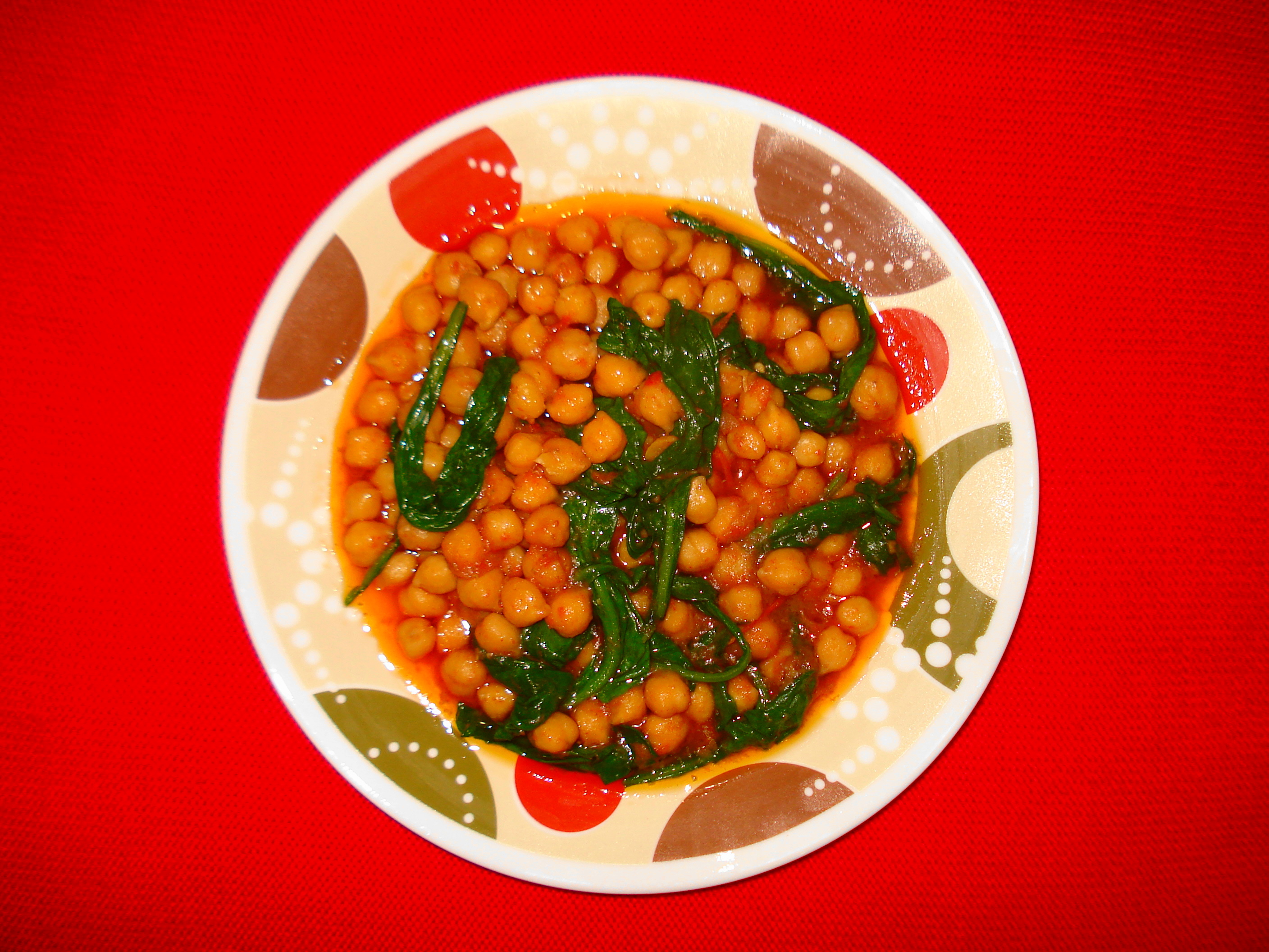 Plato de garbanzos con hojas verdes de acelga en salsa rojiza de pimentón, sobre un plato decorado