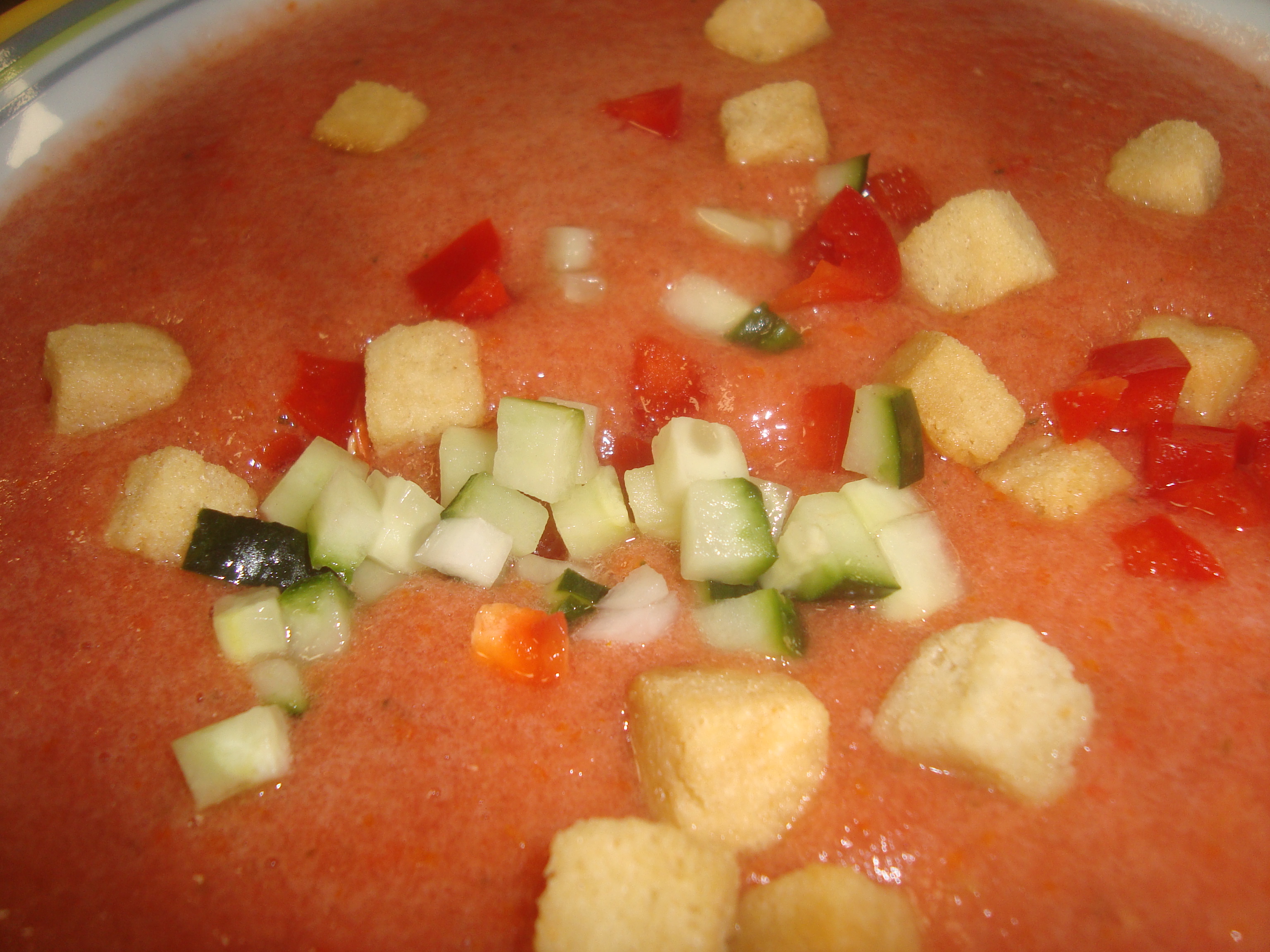 Bol de gazpacho rojo frío con picatostes, pepino y pimiento rojo picados por encima